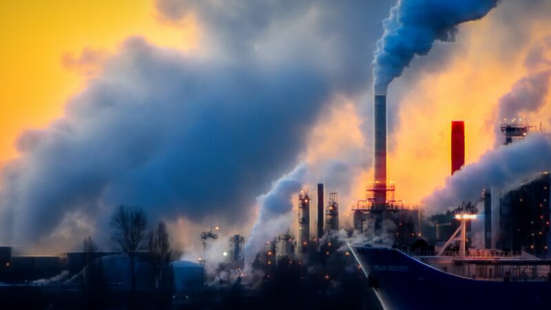 A boat in front of a factory emitting smoke