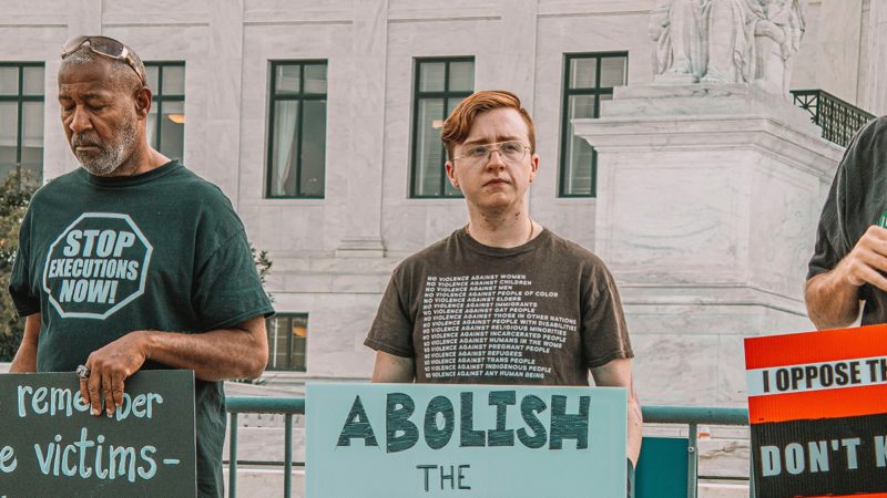 A man holding a sign says "Abolish the Death Penalty"