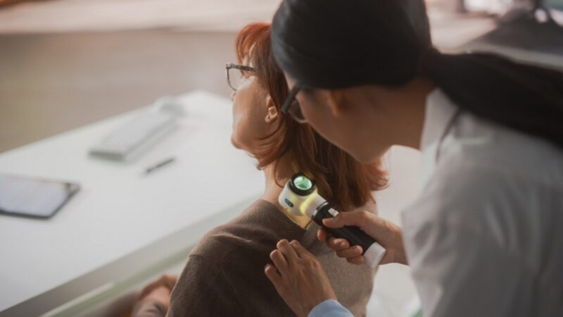 Young Asian Dermatologist is Using a Dermatoscope to Identify Worrying Cancerogenic Tissues on the Skin of a Senior Female