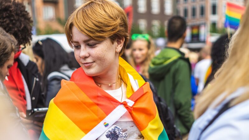 Young person with pride flag draped across back